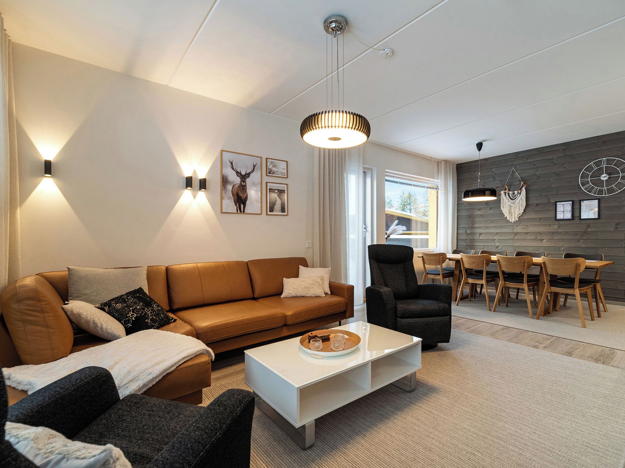 Un salon moderne avec un canapé en cuir marron, un fauteuil noir, une table basse blanche et un coin repas comprenant des chaises et une table en bois.