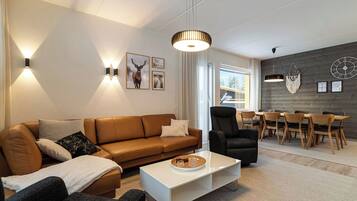 Un salon moderne avec un canapé en cuir marron, un fauteuil noir, une table basse blanche et un coin repas comprenant des chaises et une table en bois.
