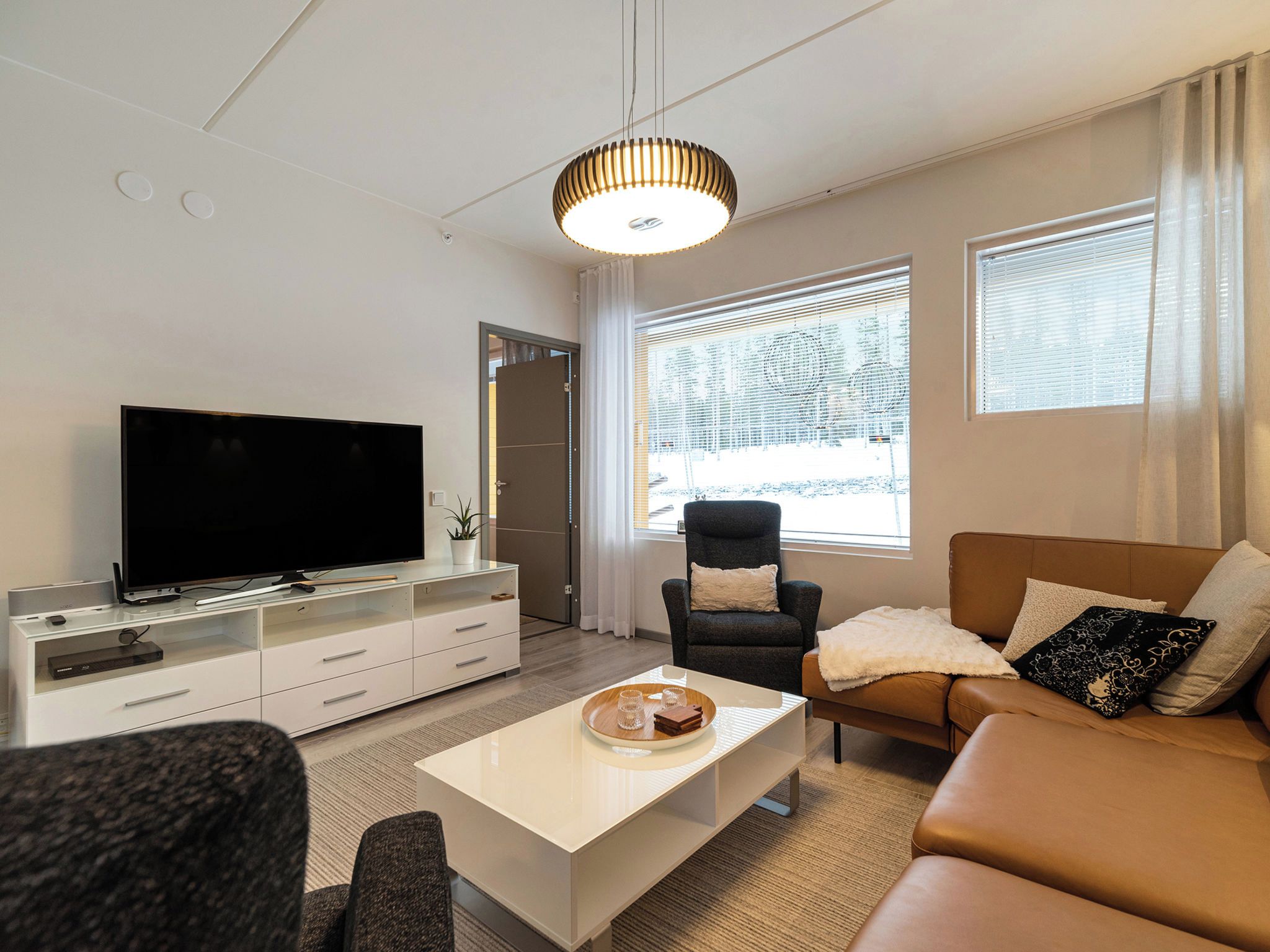 A modern living room with a flat-screen TV, a sofa, a coffee table, and a chair.