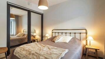 Une chambre à coucher avec un grand lit, deux tables de chevet avec des lampes, un miroir et un luminaire suspendu.