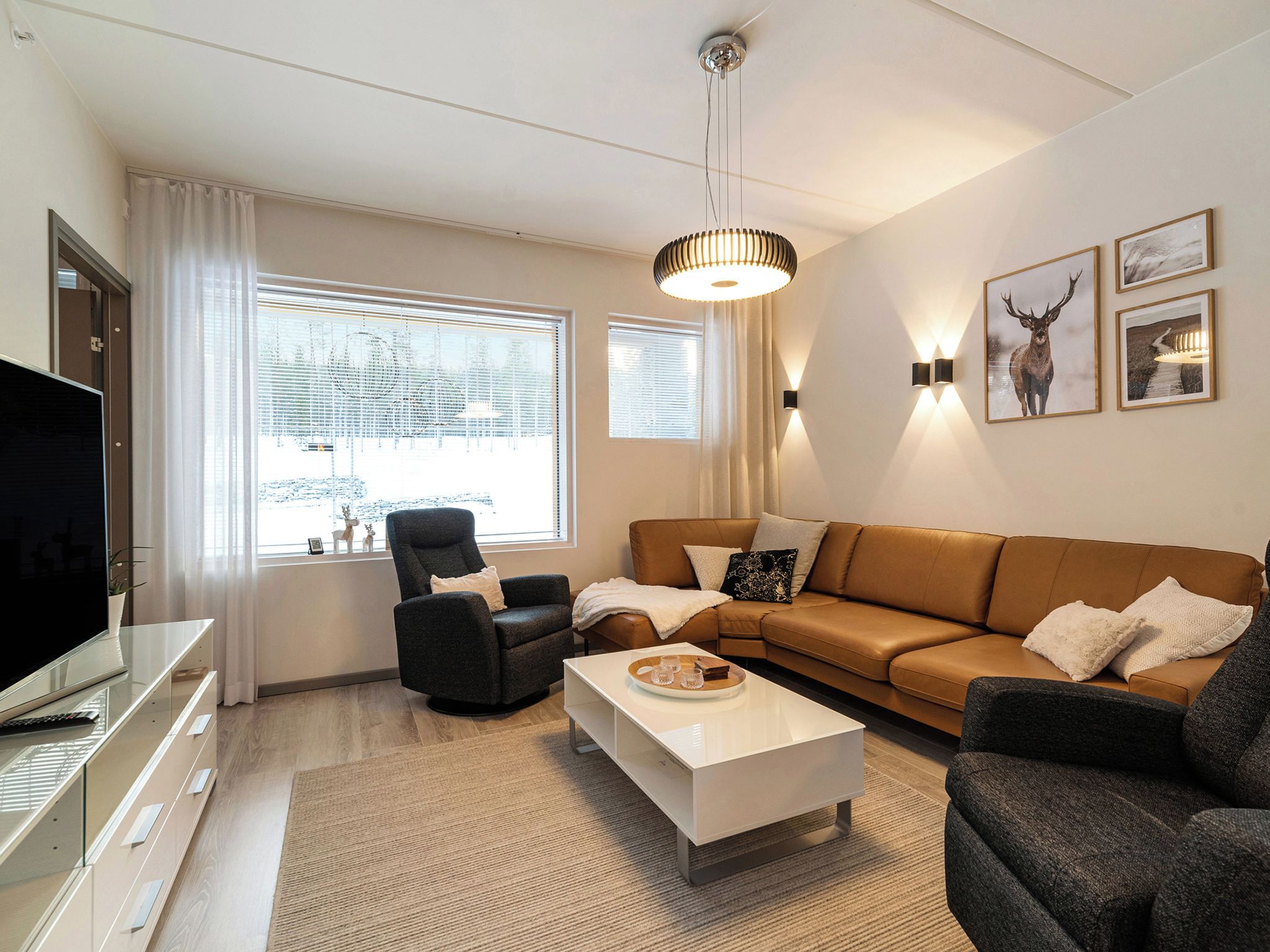En moderne stue med sofa, lænestole, sofabord og fjernsyn.