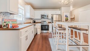 Una cocina moderna con gabinetes blancos, electrodomésticos de acero inoxidable y una zona de comedor con sillas blancas y una mesa de madera.