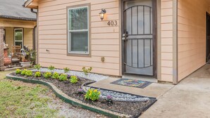 Una casa con el número 403 en la puerta, un pequeño jardín con plantas y un porche con una silla.