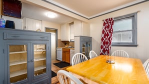 Una cocina con armarios blancos, una mesa de comedor de madera y una ventana con cortinas estampadas.