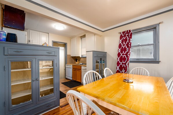 Una cocina con armarios blancos, una mesa de comedor de madera y una ventana con cortinas estampadas.
