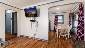 Un comedor con una mesa y sillas, un televisor montado en la pared y una puerta que da a otra habitación.