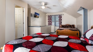 Un dormitorio con cama, ventilador de techo, ventana con cortinas estampadas y puerta.