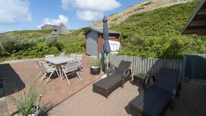 A patio with a table and chairs, a small shed, and a wooden deck. - Reetdachhaus Süderende (Hörnum (Sylt))