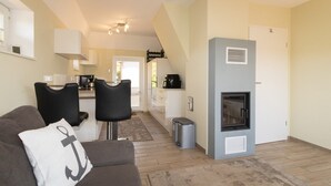 A compact living space with a sofa, two chairs, a kitchen area, and a fireplace. - Reetdachhaus Süderende (Hörnum (Sylt))