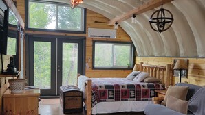 A cozy cabin interior with a large bed, a sofa, a rug with animal prints, and a wooden ceiling. - Luxurious Quonset hut in the woods, mountain views (Kila)