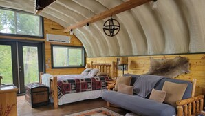 A cozy cabin interior with a bed, sofa, and a large fur rug. - Luxurious Quonset hut in the woods, mountain views (Kila)