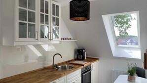 Et moderne køkken med hvide skabe, en træbordplade, indbygget ovn og et vindue med udsigt til huse.