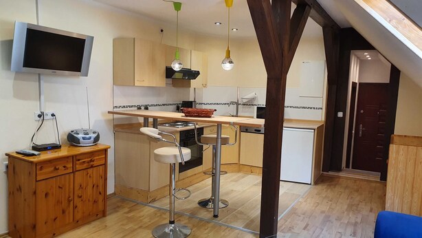 A modern kitchen with a bar area, wooden cabinets, and a TV mounted on the wall. - Vacation in the Spreewald 2 Pers - Apartment for 2 persons (Golßen)