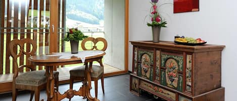 Una habitación con una mesa de comedor de madera, sillas, un armario con cuadros florales y una ventana con vistas a la vegetación.