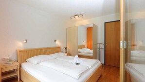 A hotel room with a wooden bed, a nightstand, a mirror, and a wardrobe. - Apartment Diedams [ground floor | 45 m²] - Apartments Susanne (Rehmen)