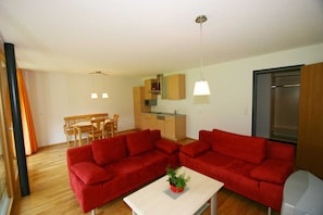 A modern living room with a red sofa set, a dining table with chairs, a kitchen area, and a large window.