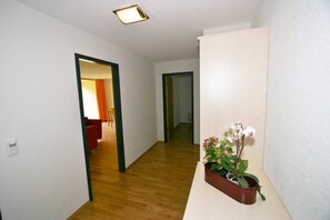 A hallway with wooden flooring, a potted orchid, and a light switch on the wall.