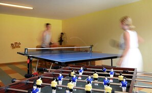 A room with a ping pong table, a foosball table, and a sofa.