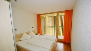 Un dormitorio con cama de madera, mesita de noche, ventana con cortinas naranjas y vista al exterior.