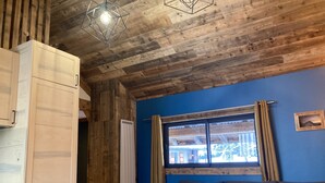 Ein Zimmer mit Holzbalkendecke, blauer Wand, einem Fenster mit Vorhängen, einer Couch und einem Tisch.