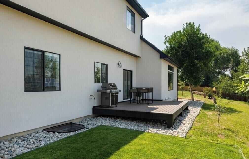 Ein modernes Haus mit Terrasse, Grill und kleiner Holzterrasse.