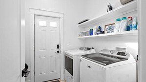 A laundry room with a white door, a washing machine, a dryer, and shelves with laundry supplies.
