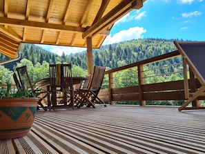 Um deck de madeira com mesa e cadeiras, com vista para uma cadeia montanhosa arborizada.