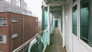 A corridor with a glass balustrade, a wooden floor, and a brick building adjacent to it. - Skyvillion Apartments - Barnet - Beautiful 2Bed Apartment with Balcony (New Barnet)