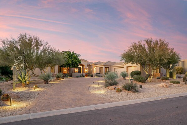 A residential property with a paved driveway, landscaped garden with cacti and shrubs, and a two-story house with a garage.