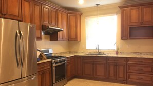 A kitchen with wooden cabinets, a stainless steel refrigerator, a gas stove, and a window with blinds.