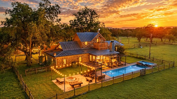 A two-story stone house with a swimming pool, outdoor seating, and string lights. - Grand Oaks Ranch · Pool·Spa · Game Barn · Animals (Fredericksburg)