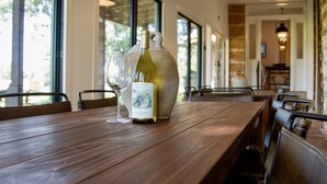 A wooden table with a bottle of wine and a glass, set in a well-lit room with large windows and modern furniture. - Grand Oaks Ranch · Pool·Spa · Game Barn · Animals (Fredericksburg)