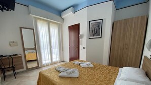 A hotel room with a bed, a wooden wardrobe, a door, and a mirror. - Hotel Nanni Garnì (Rimini)
