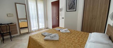 A hotel room with a bed, a wooden wardrobe, a door, and a mirror.