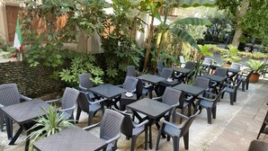 An outdoor seating area with multiple tables and chairs, surrounded by greenery and a flag. - Hotel Nanni Garnì (Rimini)