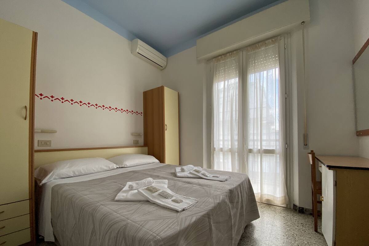 A hotel room with a bed, a wardrobe, a desk, and a window with curtains.