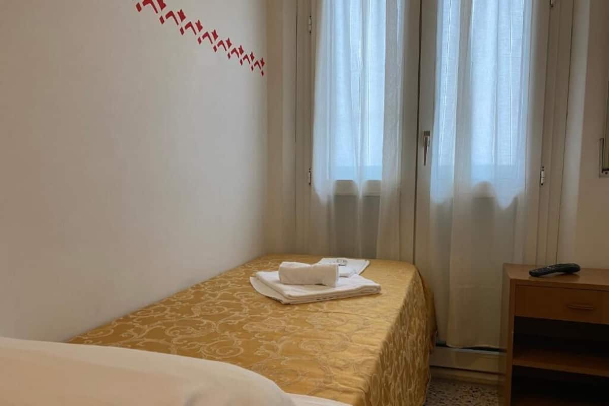 A hotel room with a bed, a bedside table, and a window with curtains.
