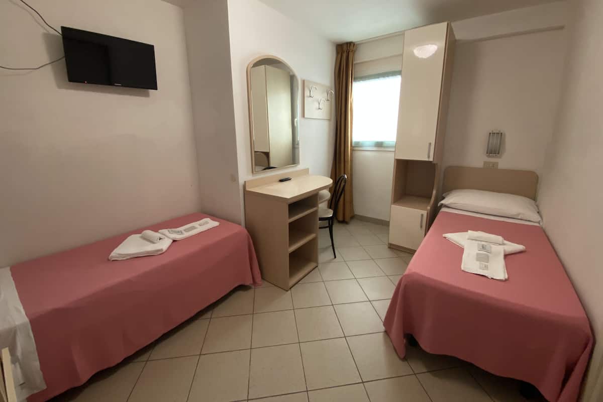 A room with two beds, a desk, a mirror, and a television.