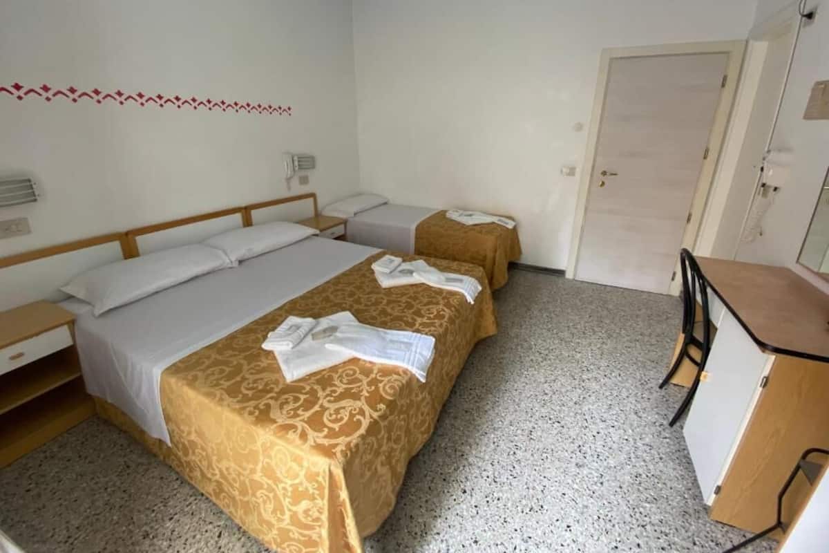 A hotel room with two beds, a desk, and a door.