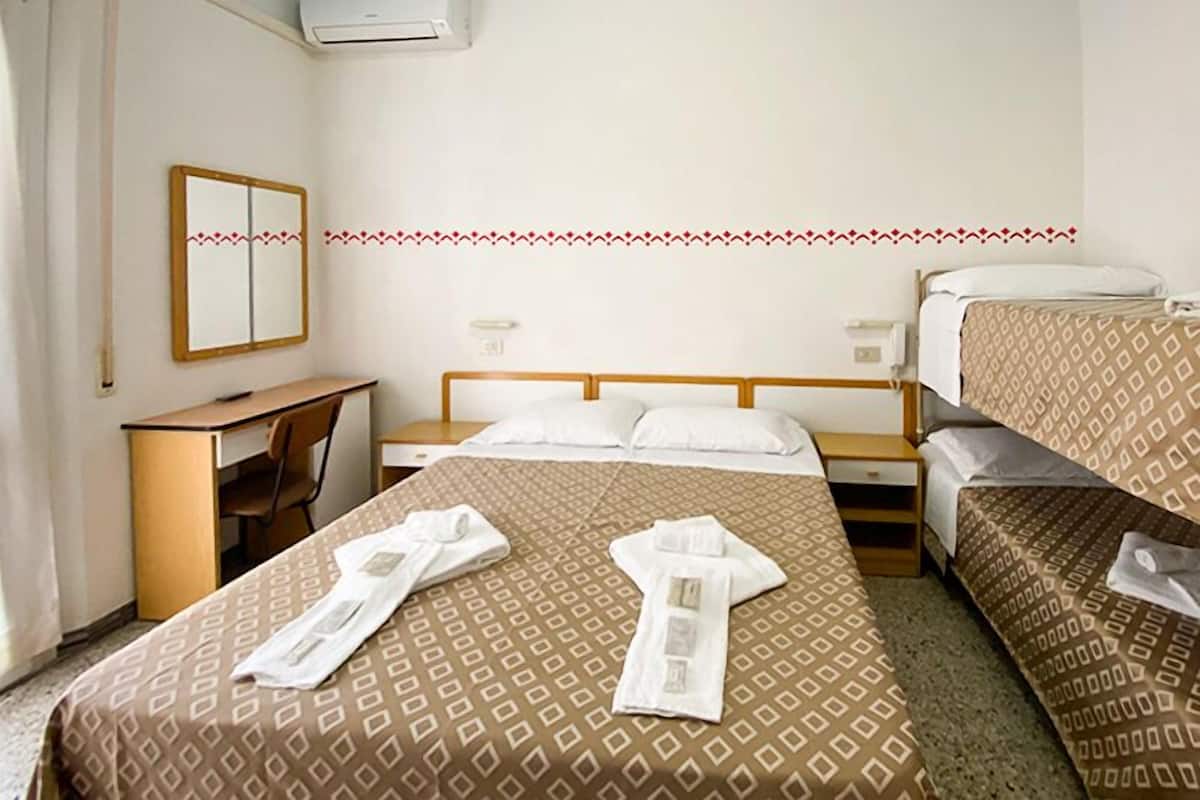A hotel room with a bed, a desk, and a mirror. There are towels on the bed.