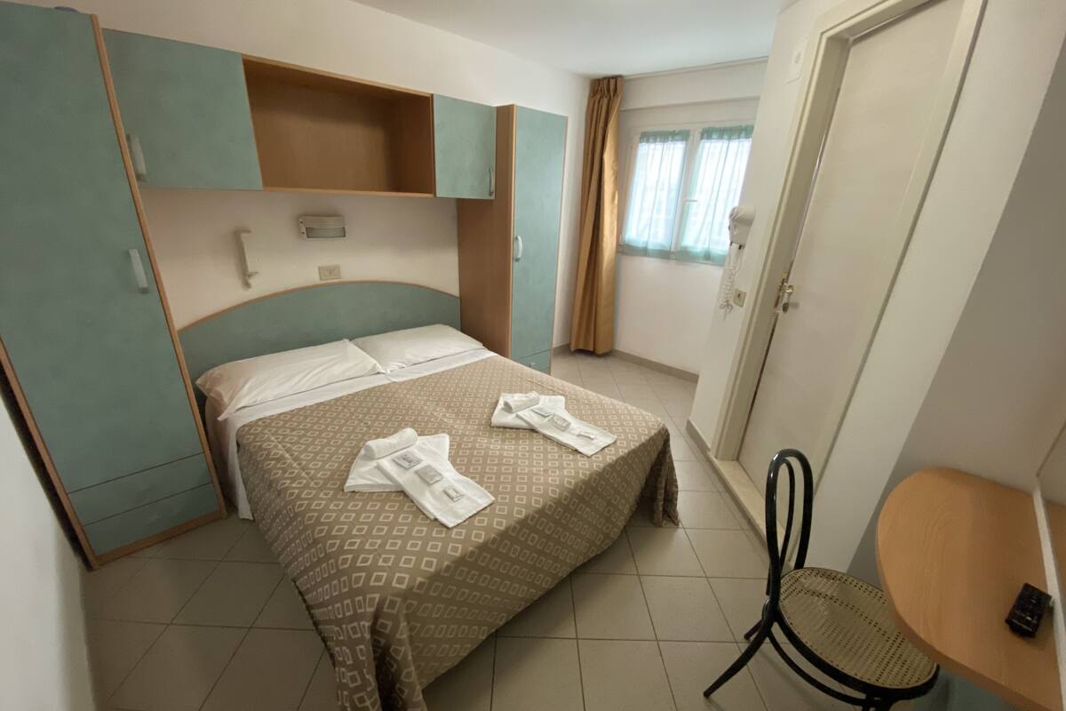 A hotel room with a bed, a chair, a small table, and a wardrobe.