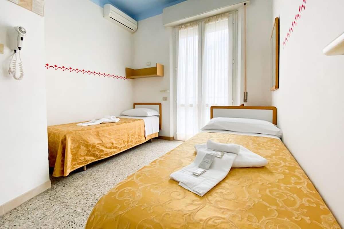 A hotel room with two beds, a telephone, and a window with curtains.