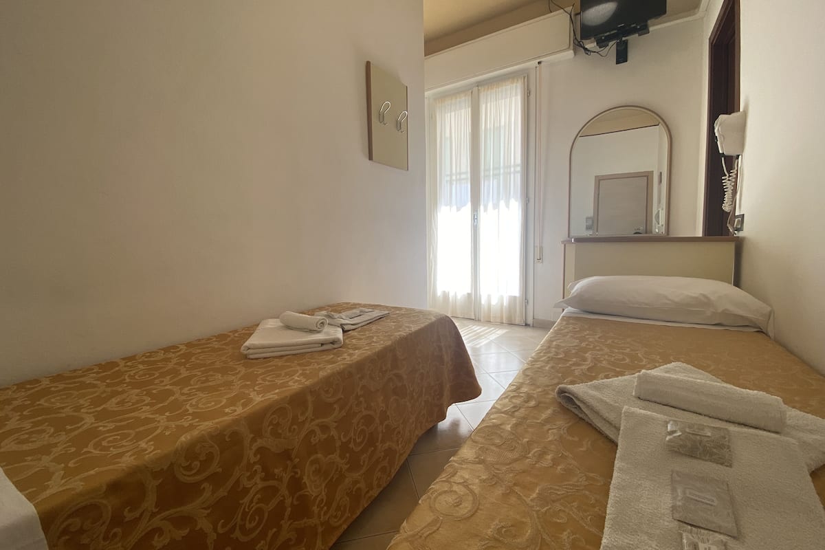 A hotel room with two beds, a TV mounted on the wall, a mirror, and a window with curtains.