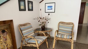 A room with two wicker chairs with striped cushions, a small round table, and a vase with dried flowers. There are framed artworks on the wall and a sign that reads "CABIN HOUSE". - Hotel Nanni Garnì (Rimini)