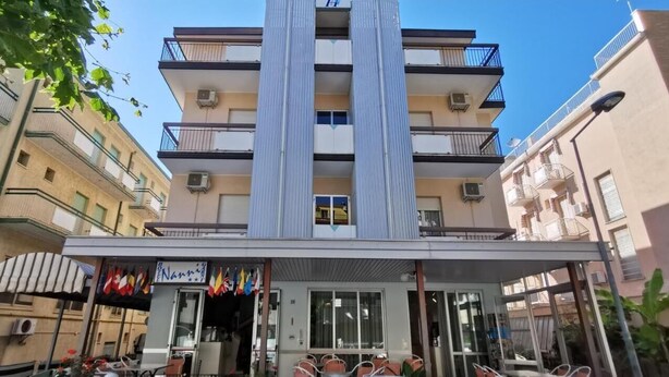 A multi-story hotel with balconies, a covered entrance, and flags. - Hotel Nanni Garnì (Rimini)
