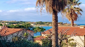 En kuststad med byggnader som har tak av terrakottafärgat tegel, ett palmtree och utsikt över havet.