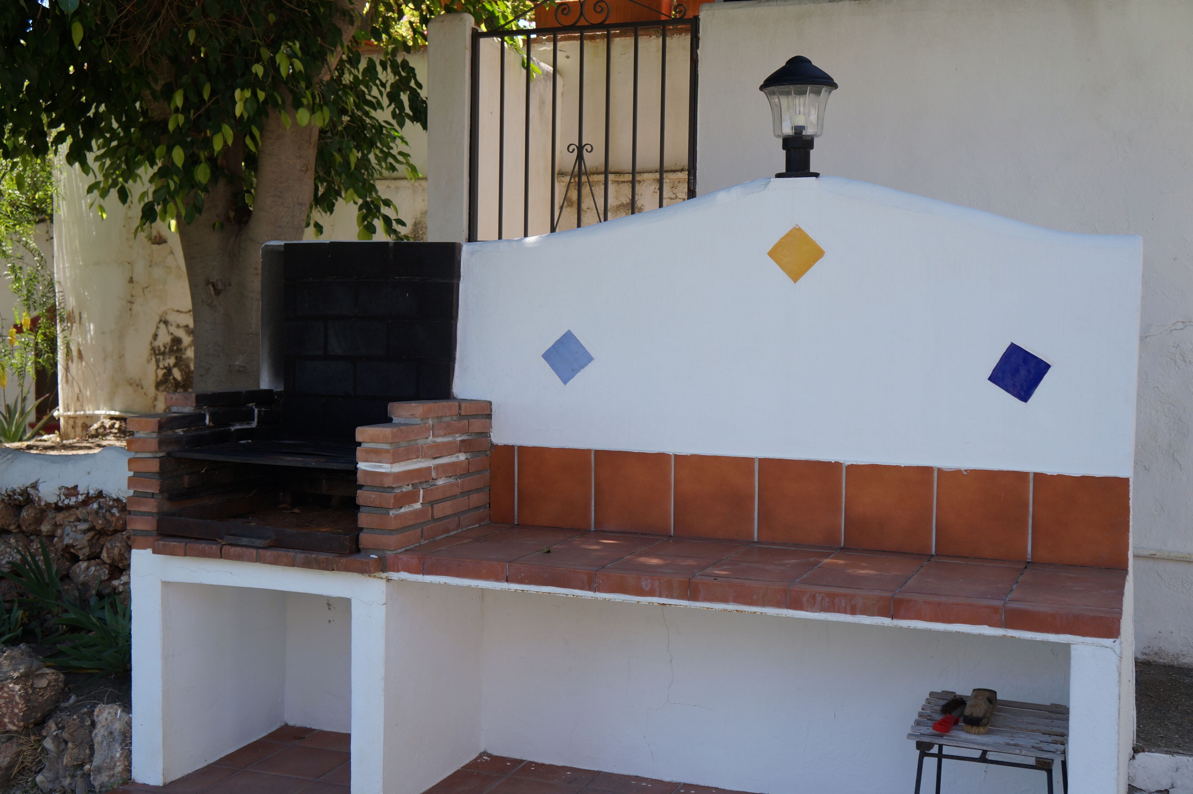 A barbecue area with a brick grill, a white bench, and decorative tiles.