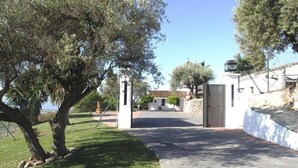 A paved driveway leading to a gated entrance with a stone wall and a building in the background. - Spectacular villa with private pool and beautiful views (Nerja)