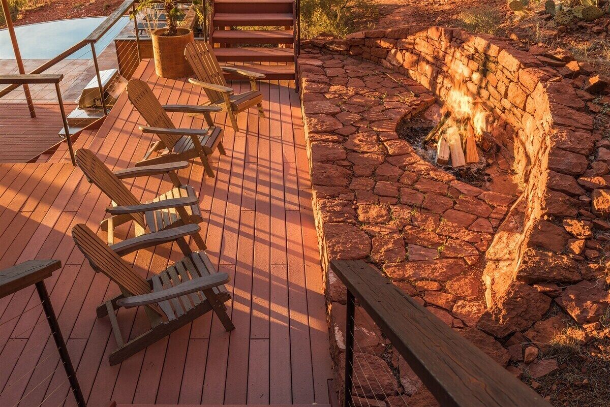 A wooden deck with Adirondack chairs, a stone fire pit, and a pool.