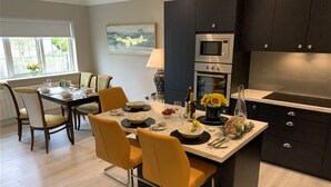 Une cuisine moderne dotée d’un îlot central, de meubles de couleur sombre et d’un coin repas avec des chaises jaunes et une table dressée pour quatre personnes.